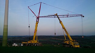 Kräne neben Windrad bei warmem Abendlicht