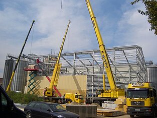 Baustelle mit drei nebeneinander positionierten Kranen beim Hallenbau