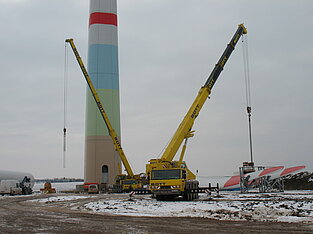 Zwei Mobilkräne neben Windkraftanlage auf winterlicher Baustelle