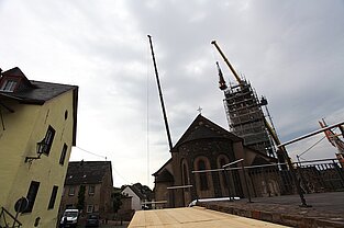 Zwei Kranarme ragen über das Kirchendach