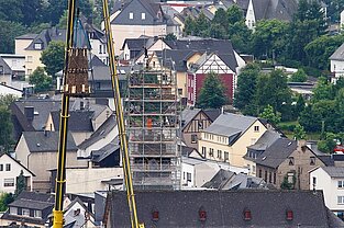 „Zwei Kräne montieren Kirchturmspitze, aus größerer Entfernung fotografiert