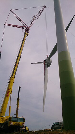 Kran positioniert Nabe mit Rotorblättern in Richtung Windrad