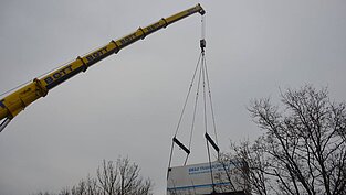 LKW-Anhänger hängt gesichert in den Seilen des Kranarms