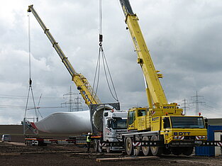 Zwei Kräne entladen Windkraftflügel von LKW auf Baustelle