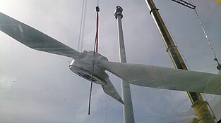 Kran hebt die Nabe mit montierten Rotorblättern zum Windradturm