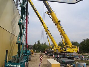 Zwei gelbe Autokräne nebeneinander auf Baustelle beim Bau der Halle