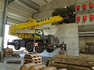 Kran mit ausgefahrenem Arm steht auf Holzunterbau, Stützen sind angehoben