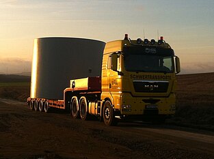 Schwerlasttransporter transportiert Windanlagenteil bei Sonnenuntergang